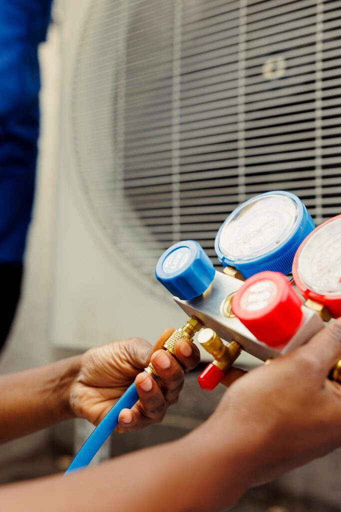 HVAC technician checking an outdoor air conditioner’s refrigerant pressure with manifold gauges.