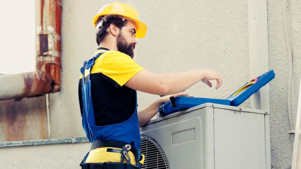 HVAC technician inspecting and servicing an outdoor heat pump unit with a tool kit.